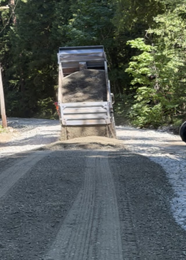 A dump truck dumps gravel onto a gravel road bed in a forest
