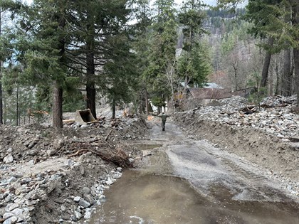 A person on a cleared path among piles of mud, rocks, and debris as high as their shoulders.