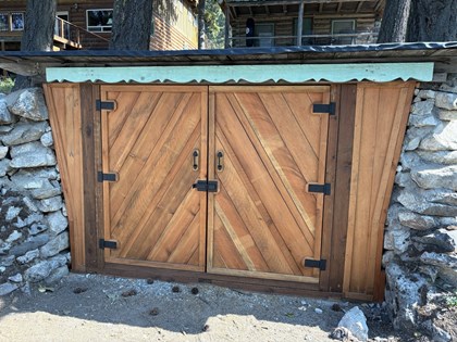 Two wood panel doors set in a casing flanked by stone walls. Bottom of doors is at ground level.