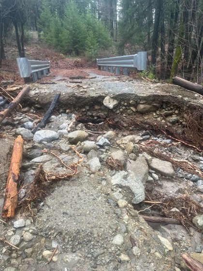 A dirt road bed bisected by ditch full of rocks and other debris. Beyond are two bridge railings.