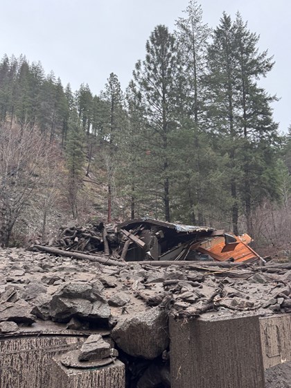 Wreckage of a collapsed building and foreground structure partially buried in mud, rocks, and debris.