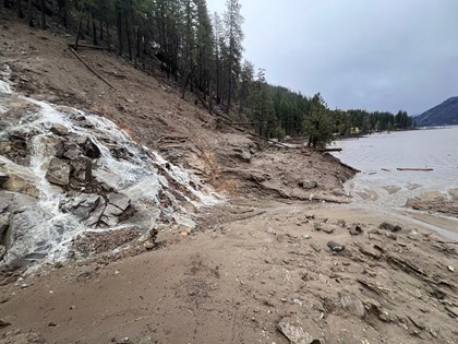 Water cascades down a dirty and rocky slope draining into a forest edged lake.
