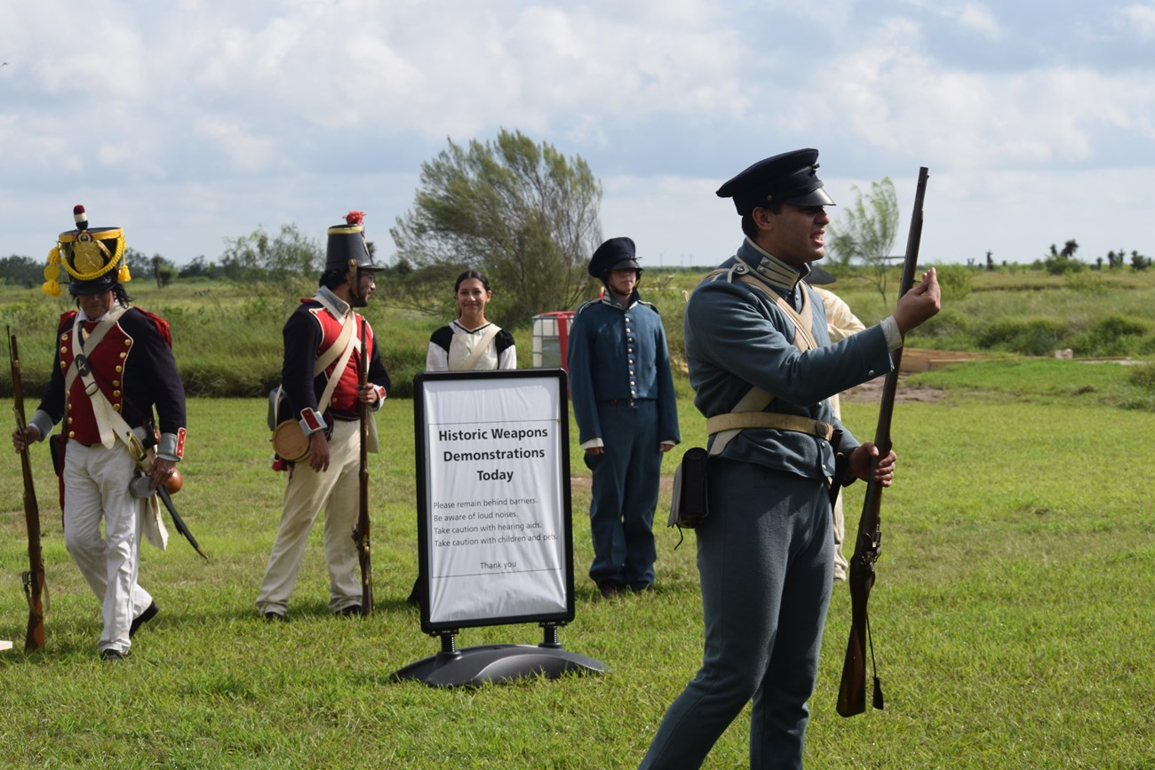 Volunteer in a US infantry uniform describes Muskets used in the US-Mexican War. Other volunteers dawning historic attire stand in a line behind him.