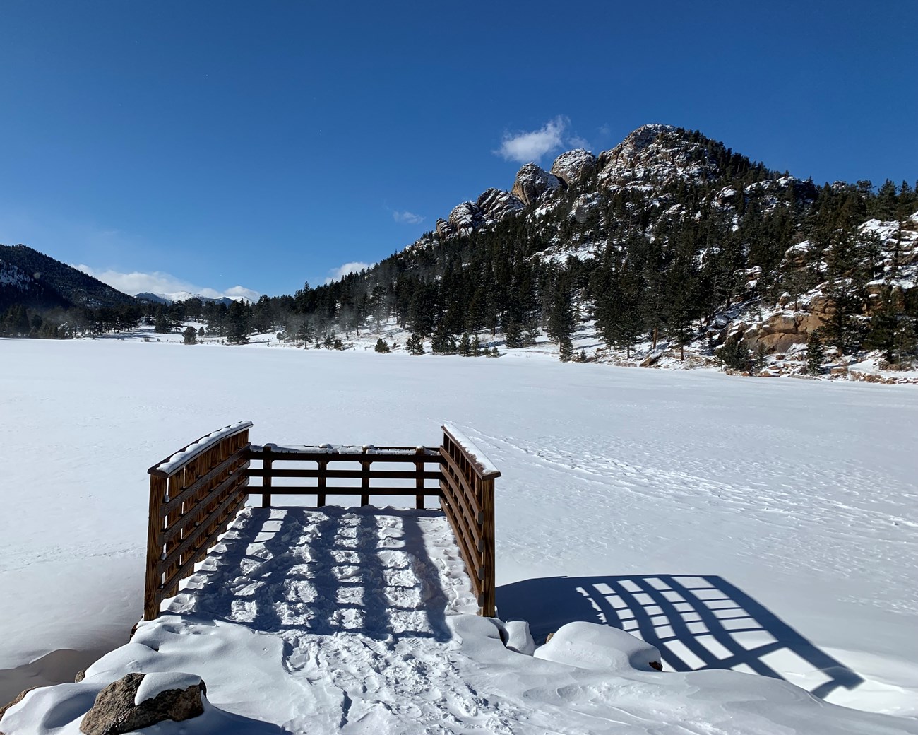 Small dock on a snow-covered lake with mountains.