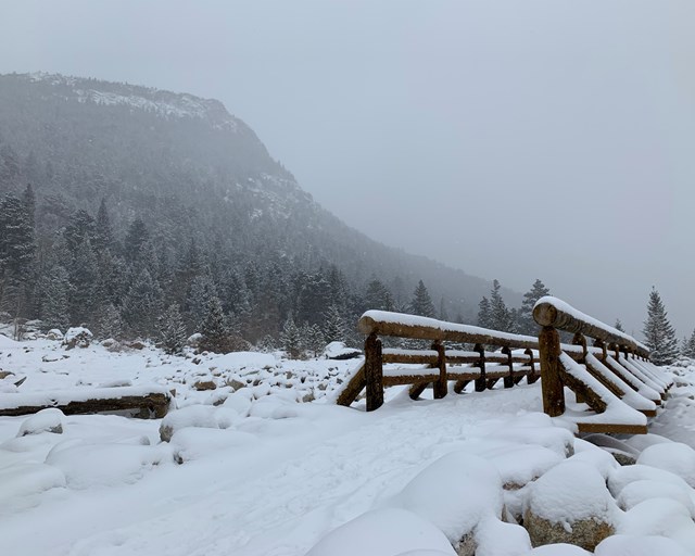 Wooden footbridge covered in snow surrounded by rocks and mountains.