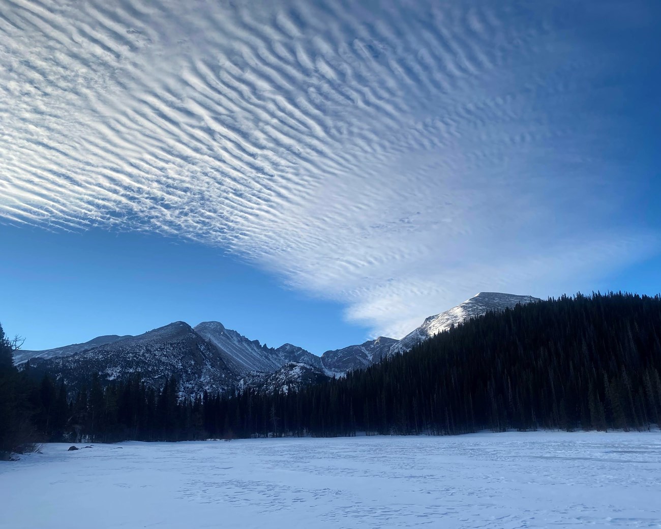 Frozen winter lake with rippling clouds and mountains.