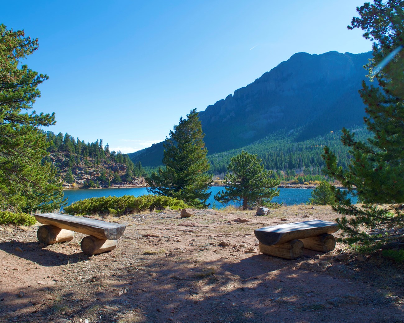 Two benches overlooking lake on top of a small hillside.