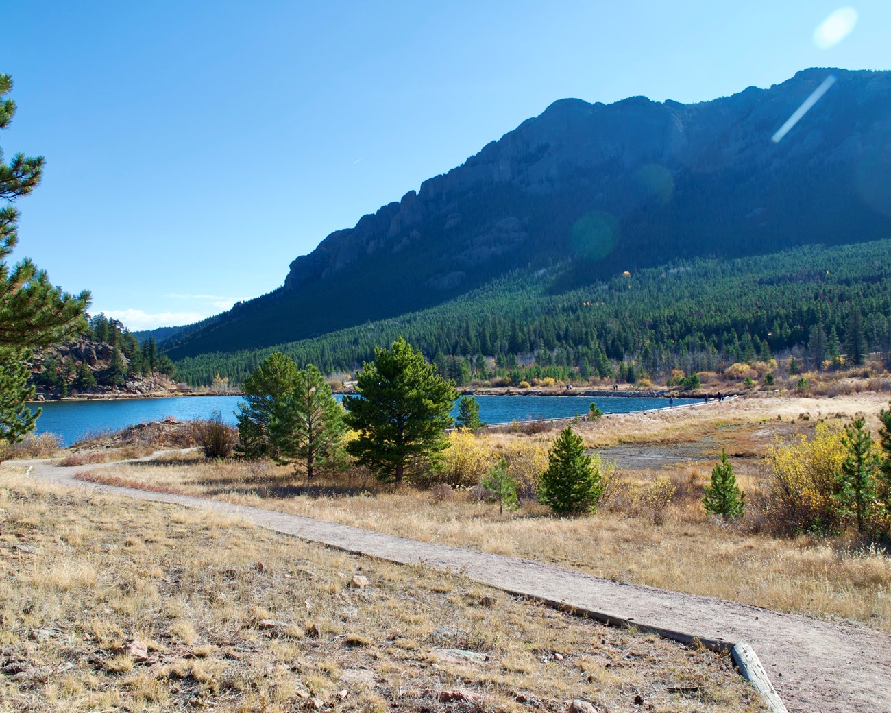 Dirt trail going towards a lake surrounded by mountains.