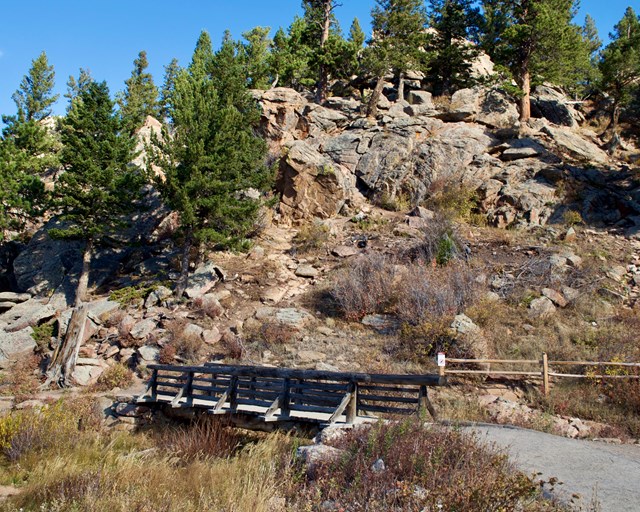 Wooden footbridge next to rocky hillside.