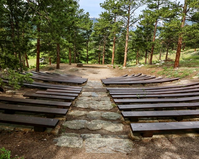 Amphitheater with wooden benches, uneven stone steps, and dirt platform.