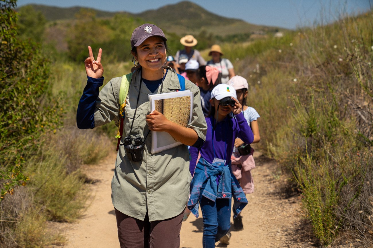 An education technician guides a group of 4th graders down a trail in the great outdoors.