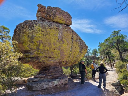 Hikers stand under huge yellow rock that resembles a submarine