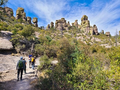 hikers on a trail under pinnacle rocks with trees