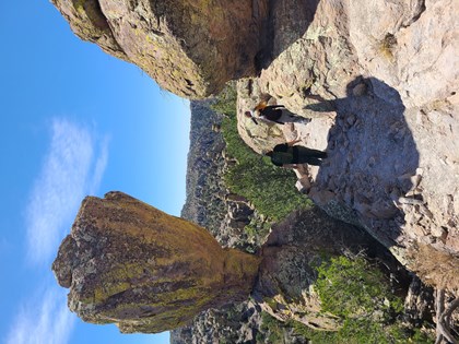 hikers stand on trail under large rocks