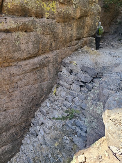 man standing above large boulders below high cliffs