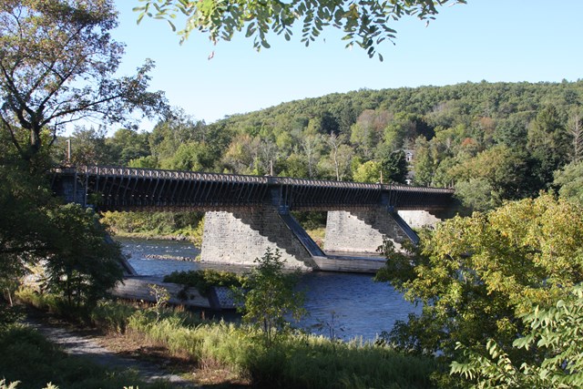 bridge with stone supports and wooden icebreakers over a river. Bridge is made of wooden trusses.