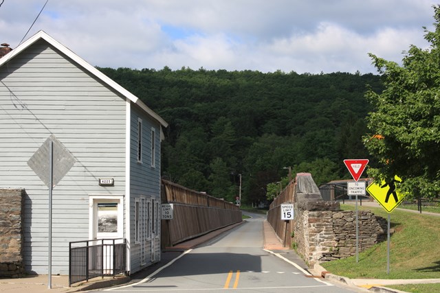 Head-on view of an aqueduct converted into one-lane vehicular bridge. On left is a blue building.