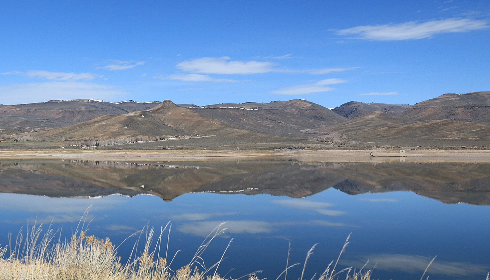 Historic black and white image of a train passing through a valley with mesas in the background