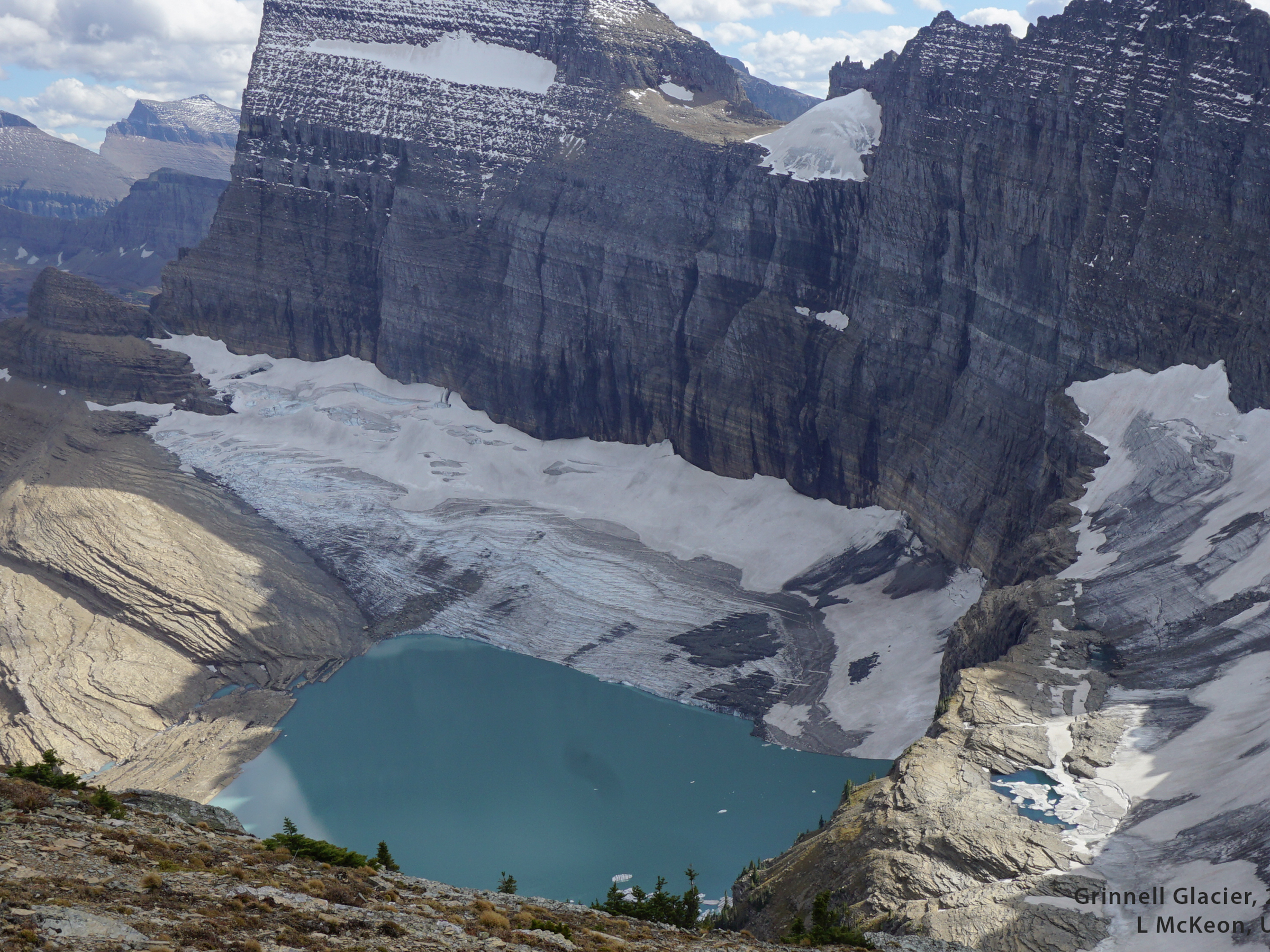A mountain glacier tucked against a mountain with a lake forming at its front.