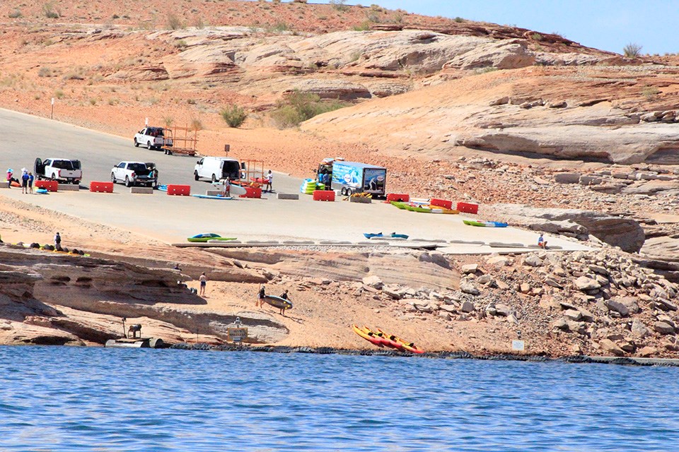 Various kayaks and gear on launch ramp. rocky shelf to water.
