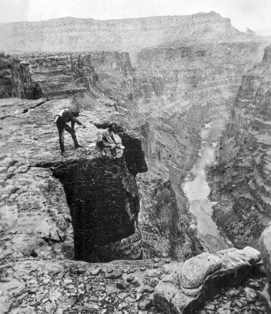 Two men on edge of cliff with river below.