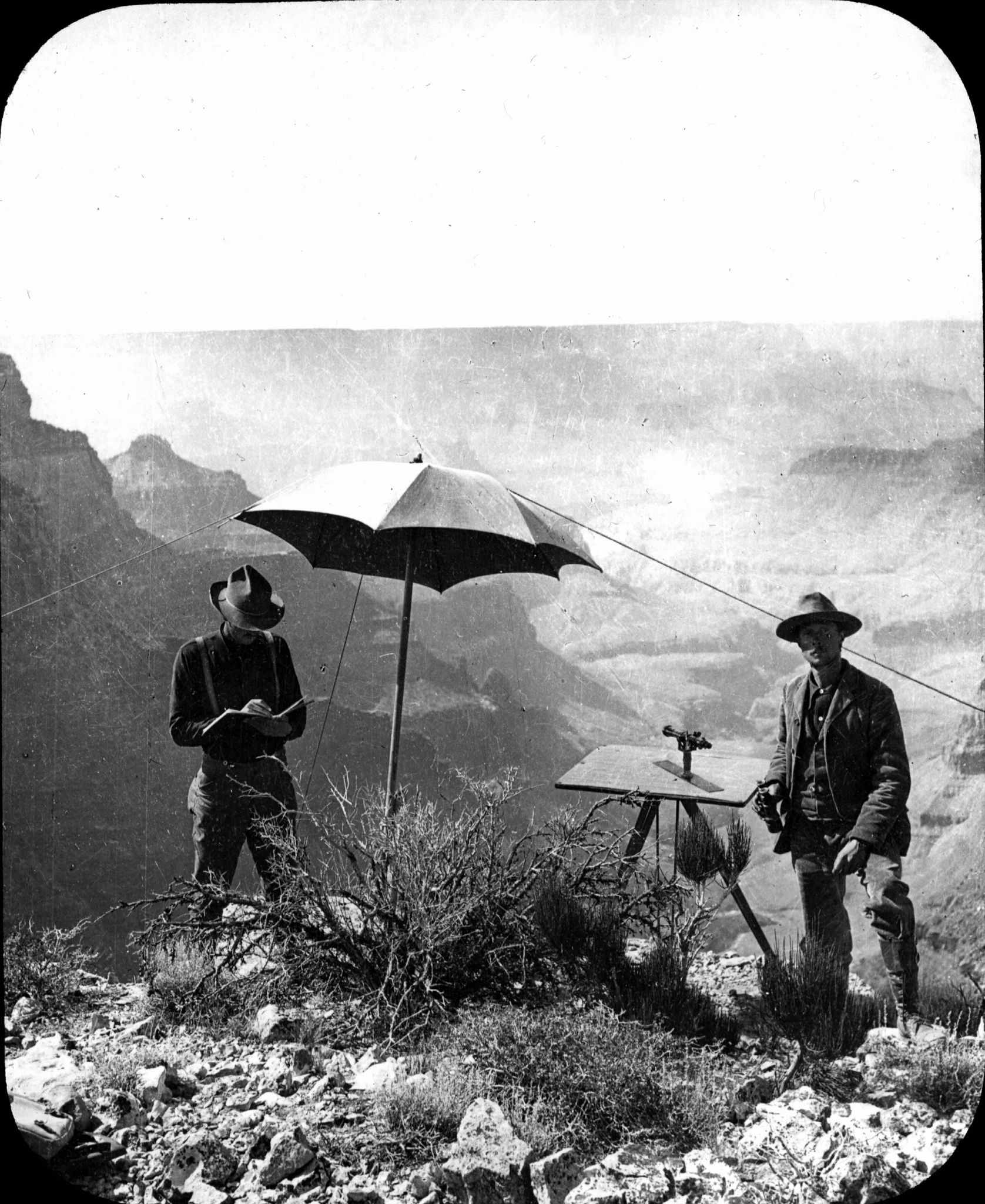 Photo of two men with topographical equipment on edge of cliff
