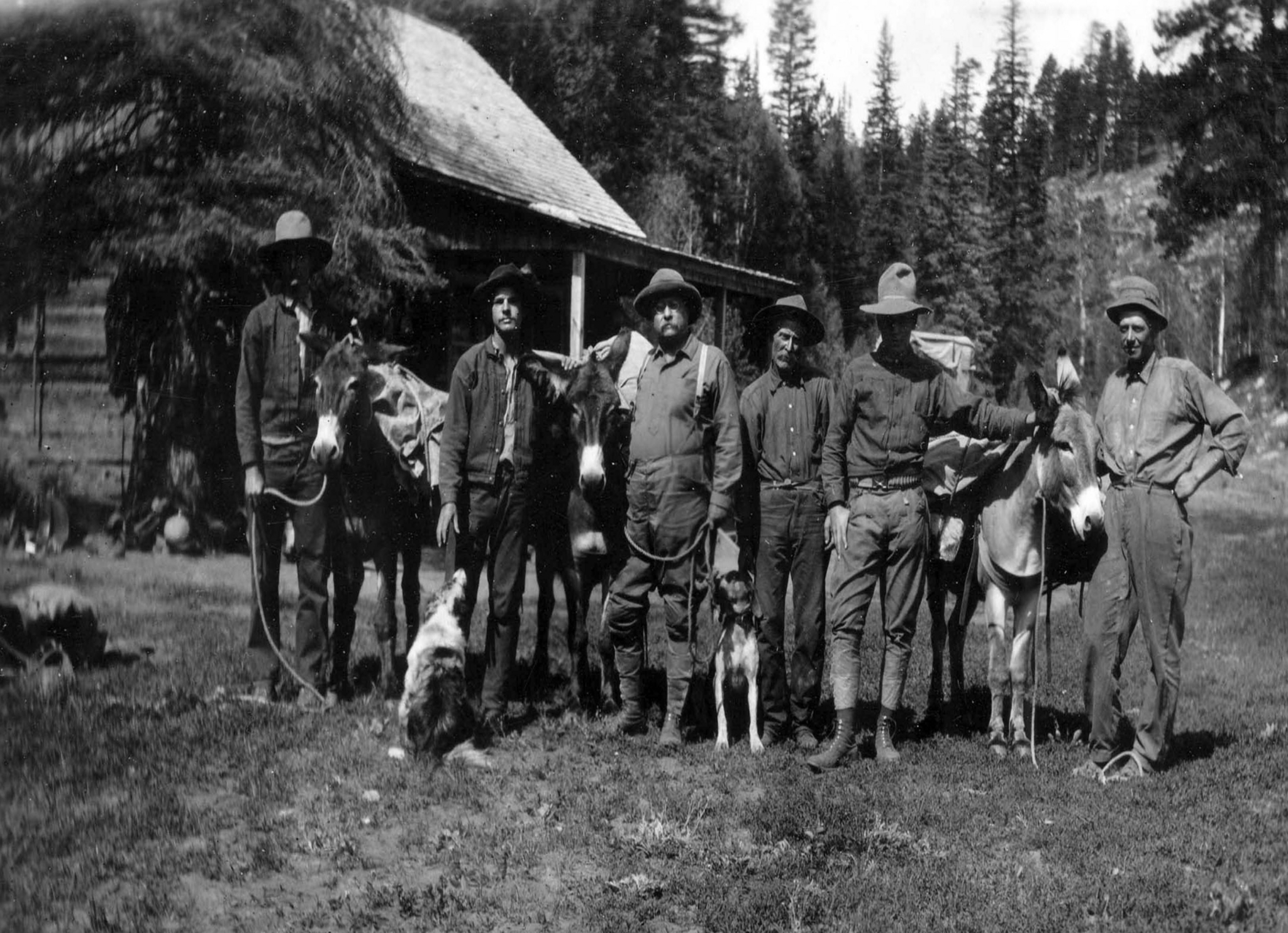 A group of men, a dog, and a burro in front of a cabin.