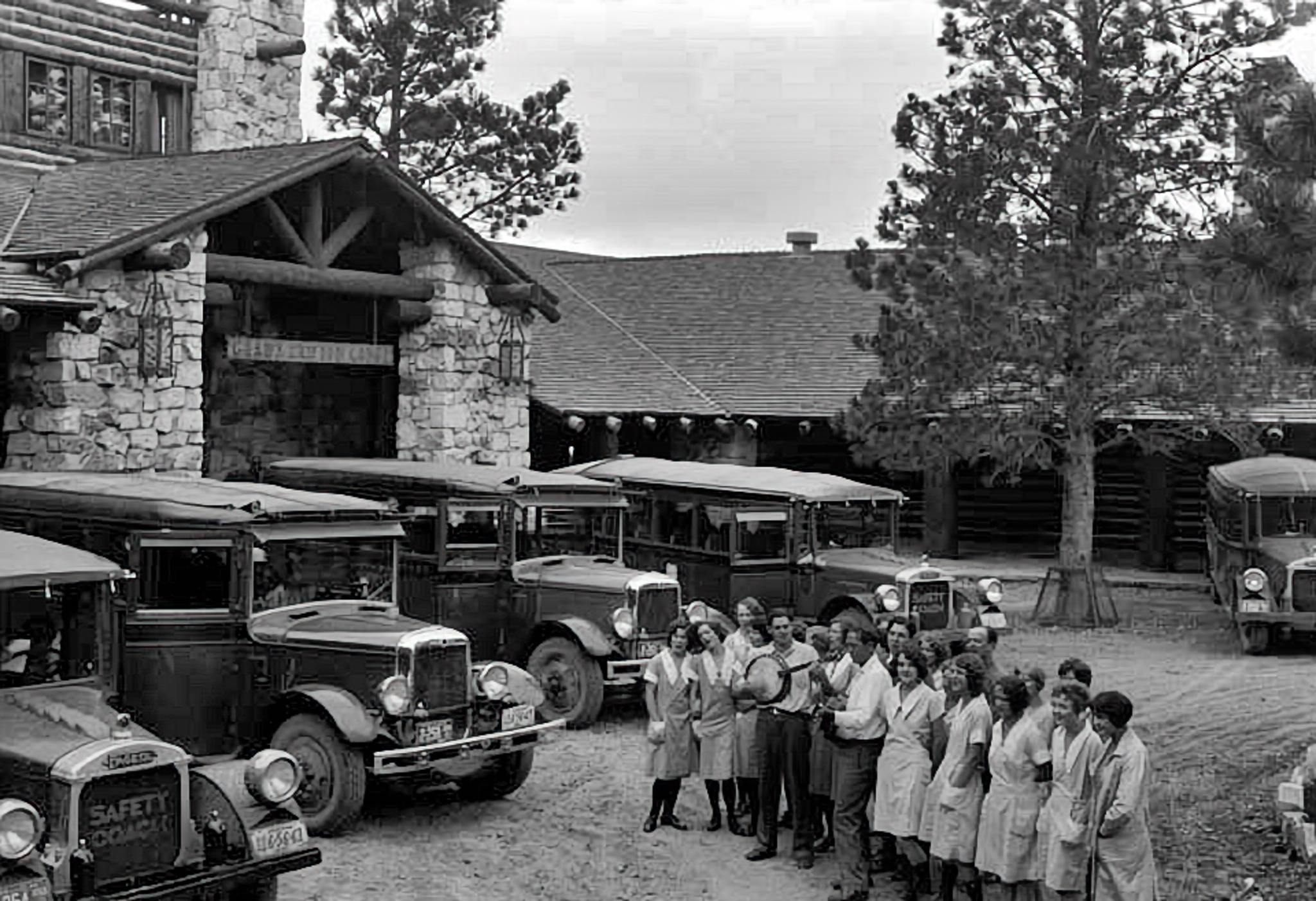 Old cars with group of people lined up in front of hotel building.