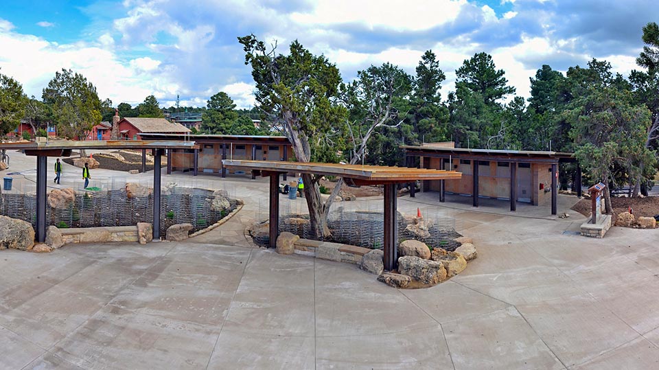 An undeveloped area next to the Bright Angel Trailhead shows the ground, trees, and four Porta-a-potties.
