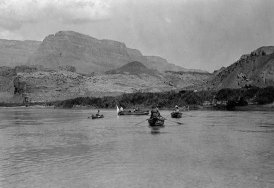 People in boats on river with cliffs and trees
