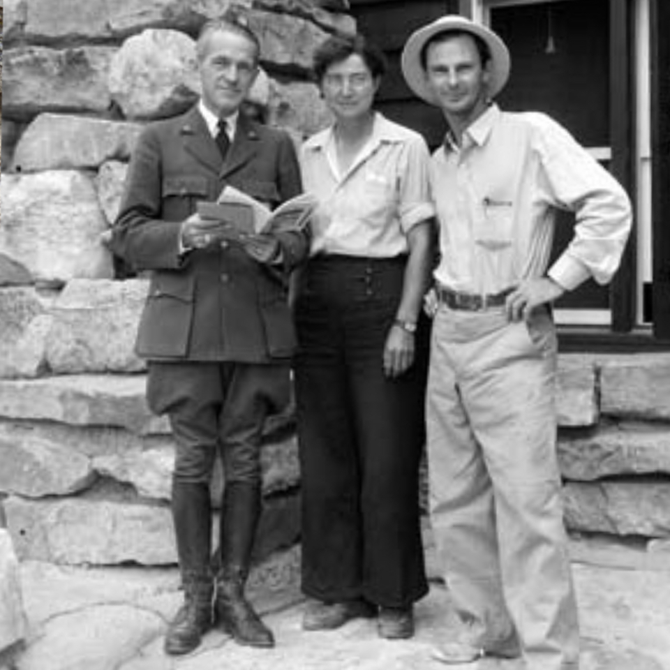 Two men and a woman stand next to stone building and window