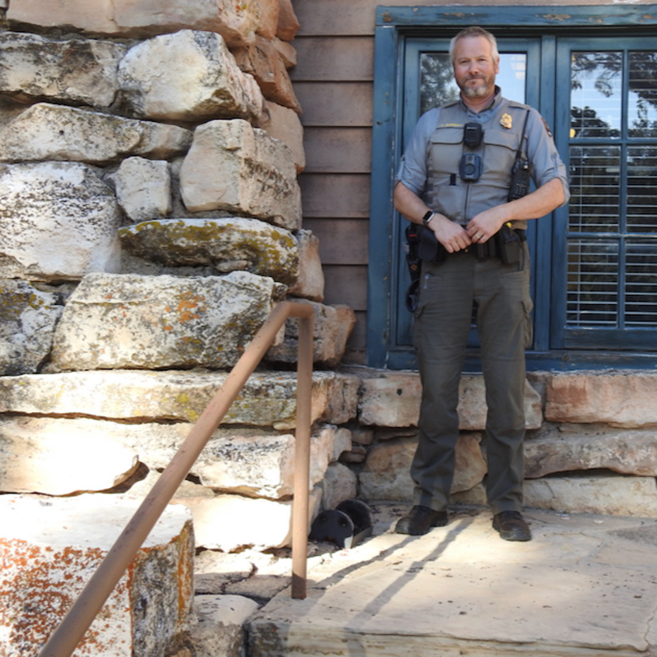 Two men and a woman stand next to stone building and window