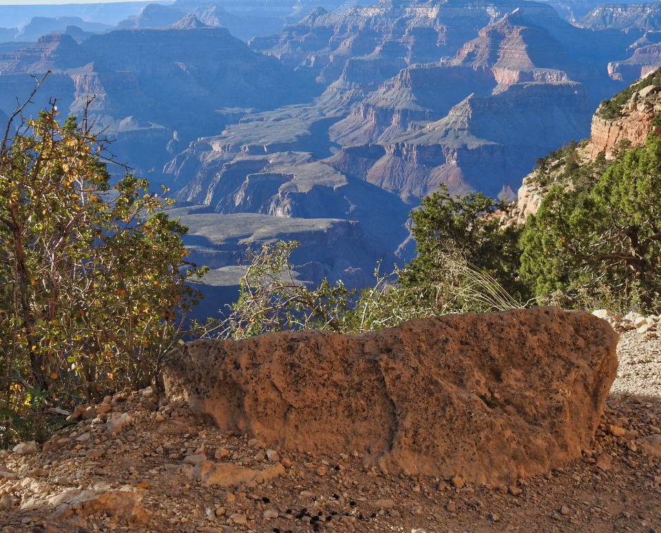 Man with backpack sitting on rock on trail looking down into canyon