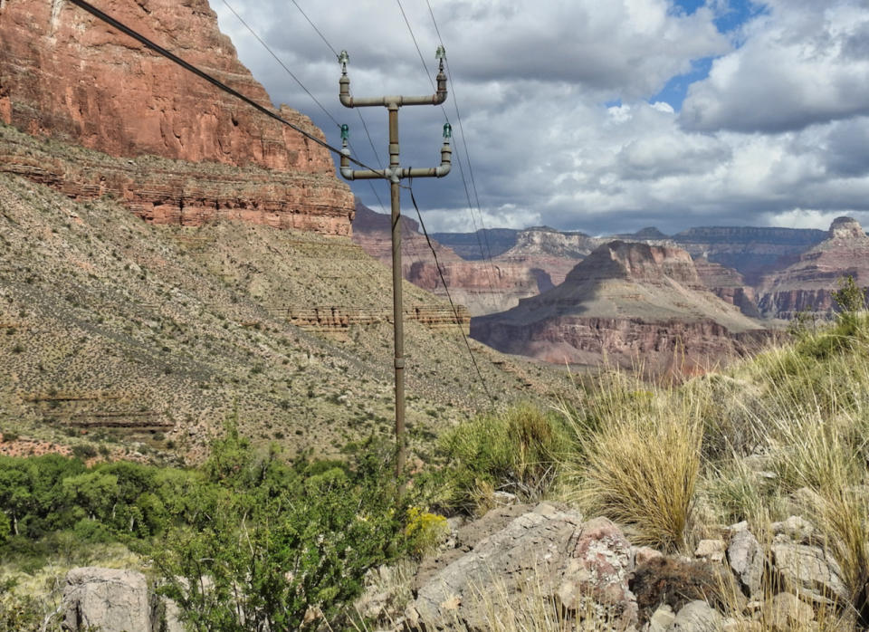 Two men, one atop a pole, the other holding it steady. Cliffs in background