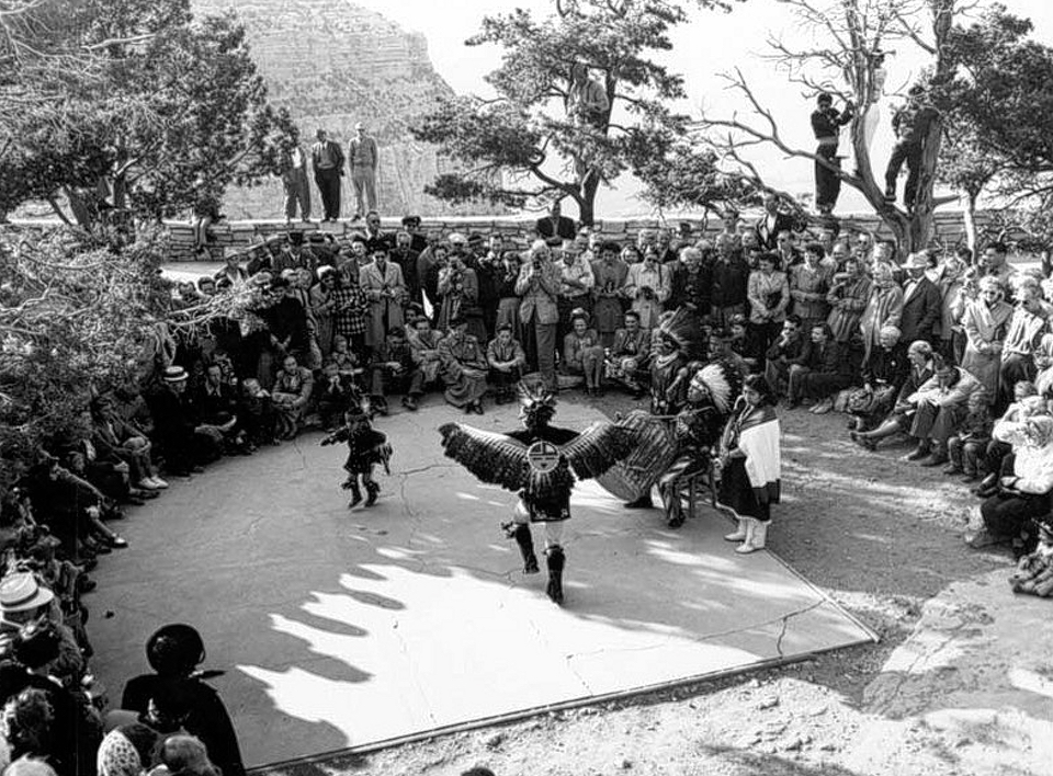 People in Native American ceremonial clothing dancing with others watching.