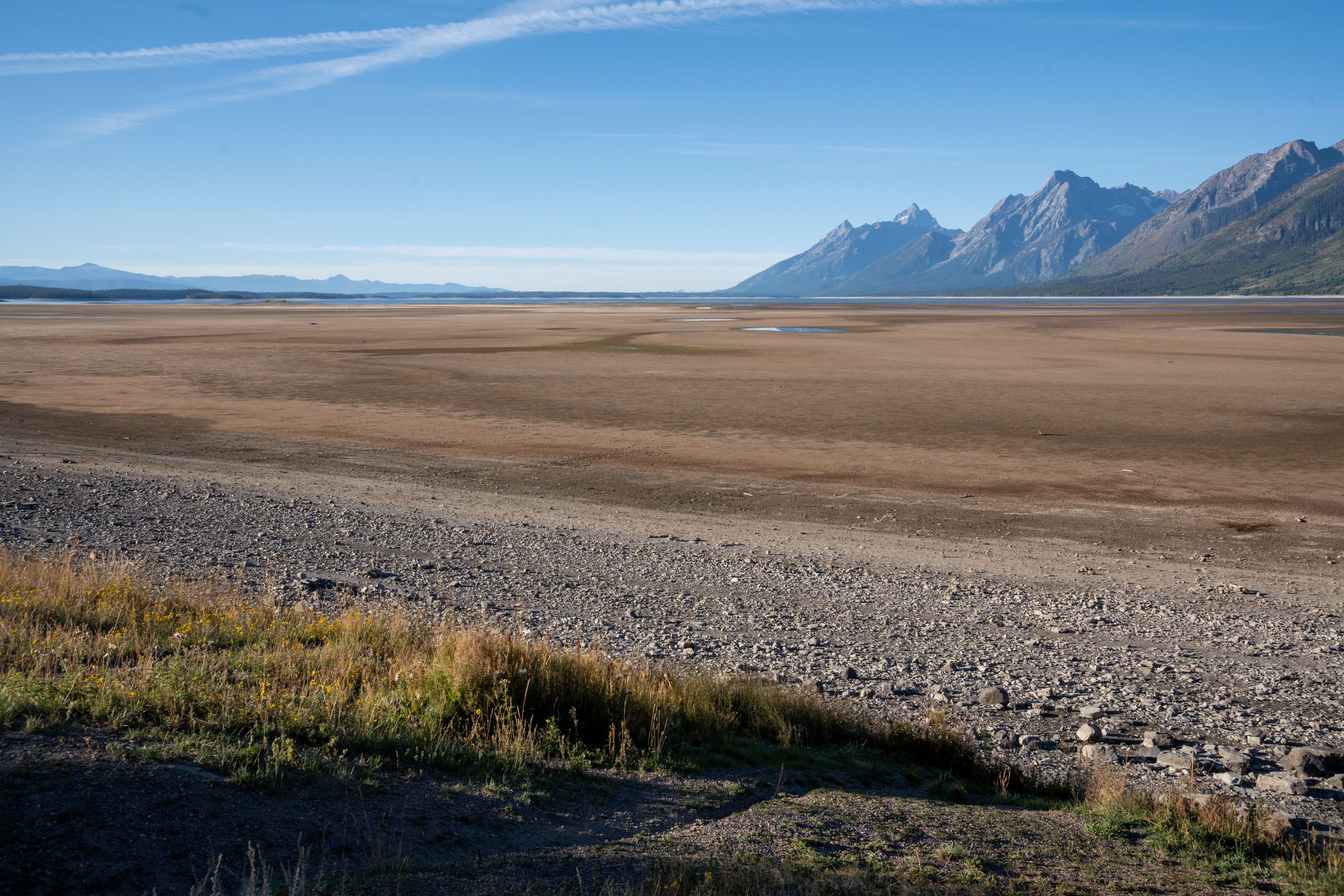 Visitors stand near the edge of a lake with the teton range in the distance.
