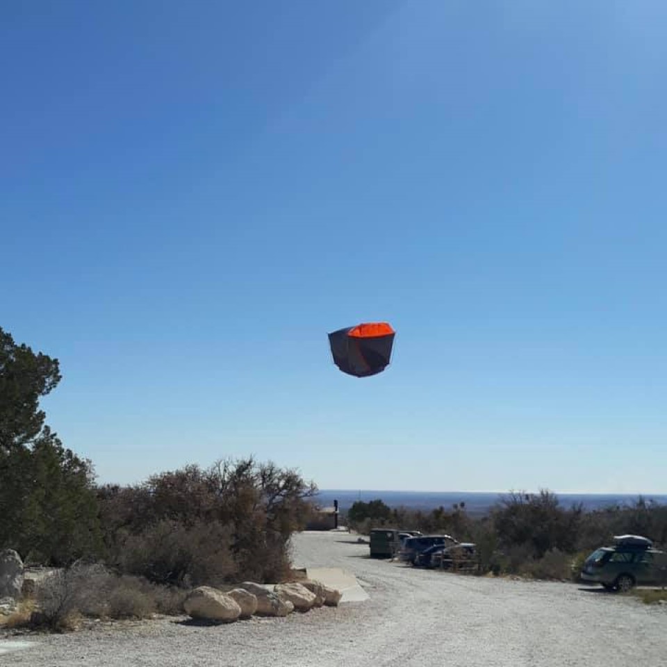 A dome tent is suspended upside down about twenty feet off the ground in high winds