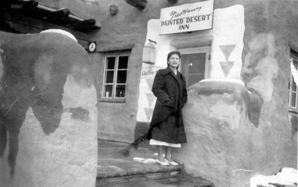 Old photo with girl in dark coat in front of a pueblo style building
