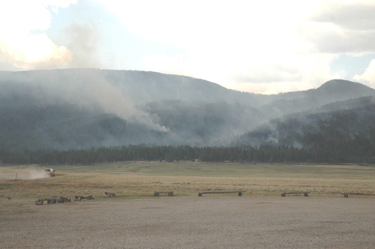 Smoke rises from a wildfire on a forested mountain.