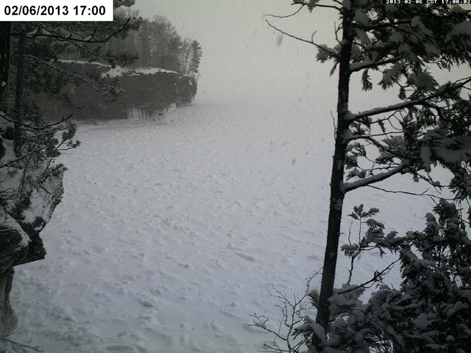 Upper left corner: White box with black text that reads 02/06/2013 17:00. A snow-covered frozen lake stretches between two cliffs and far out into the distance. No water visible.