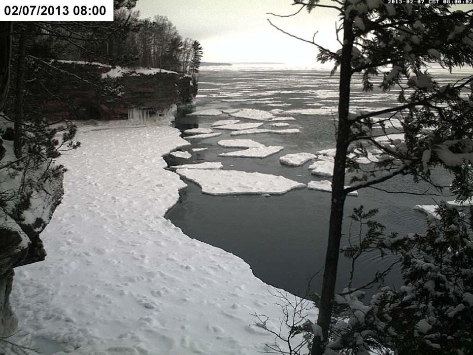 Upper left corner: White box with black text that reads 02/06/2013 17:00. A snow-covered frozen lake stretches between two cliffs and far out into the distance. No water visible.