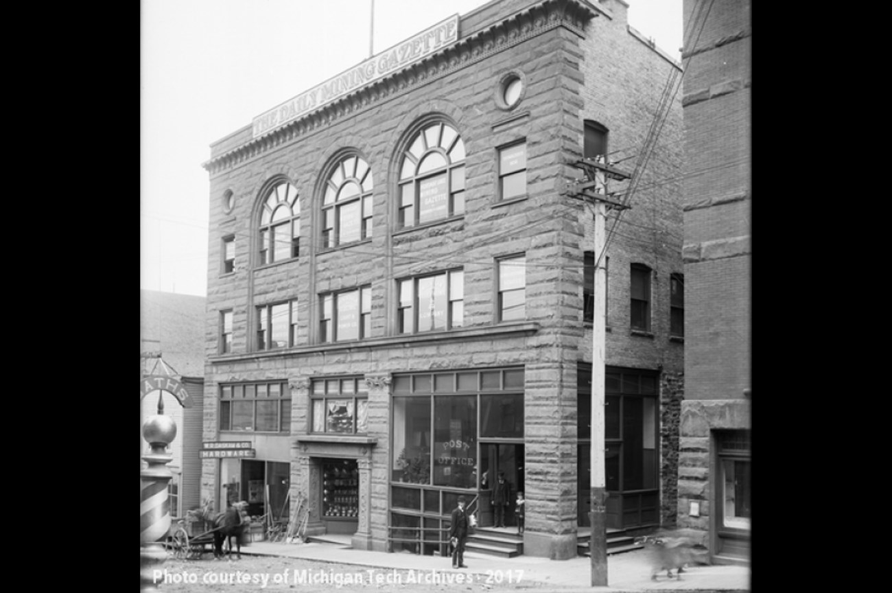 A historic back and white photo of a three-story brick and sandstone building in Calumet, MI