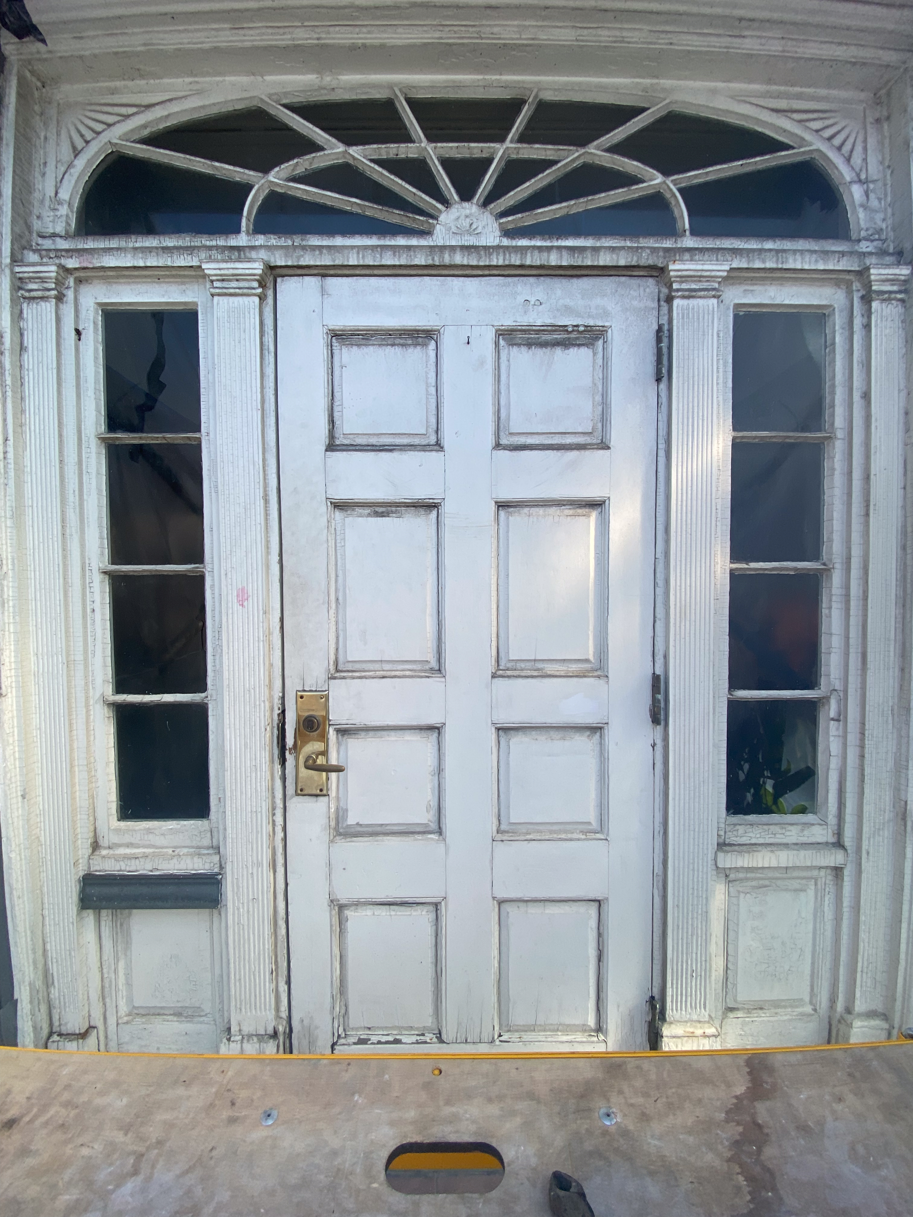 A large white door with top and two glass side panels in worn condition.