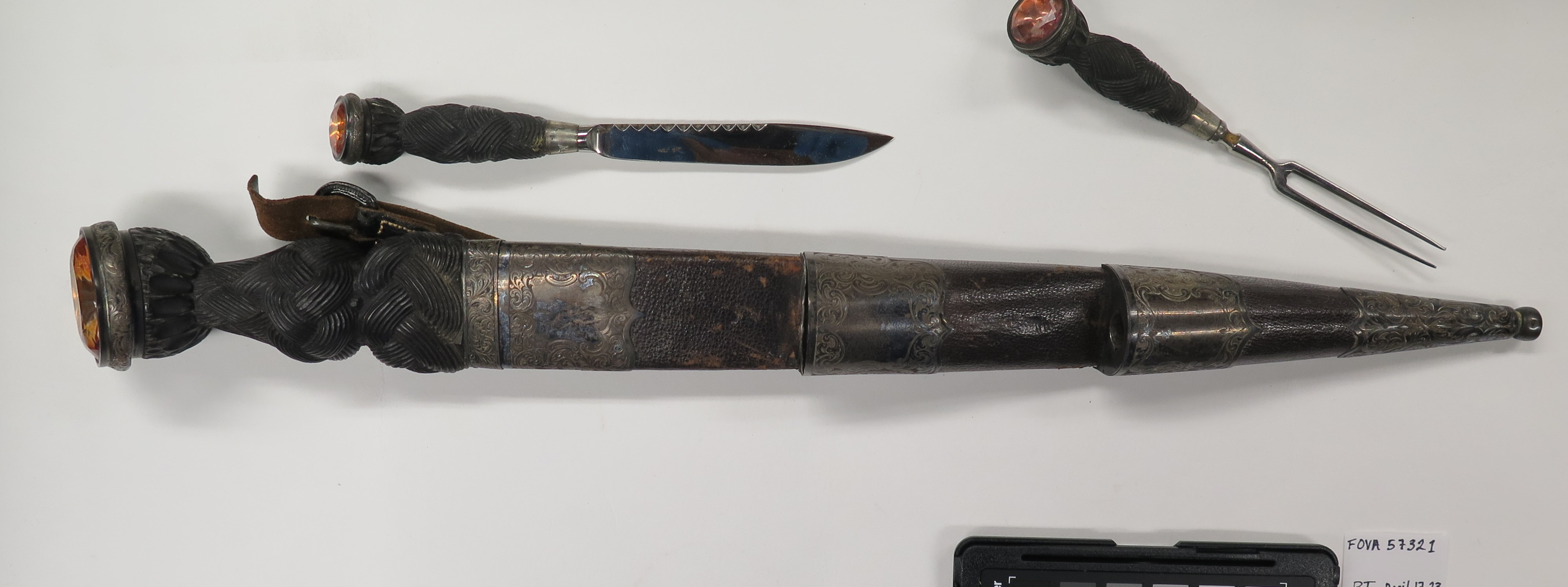 A dagger in a sheath, small knife and fork. All are dull and tarnished with orange gemstones on their hilts.