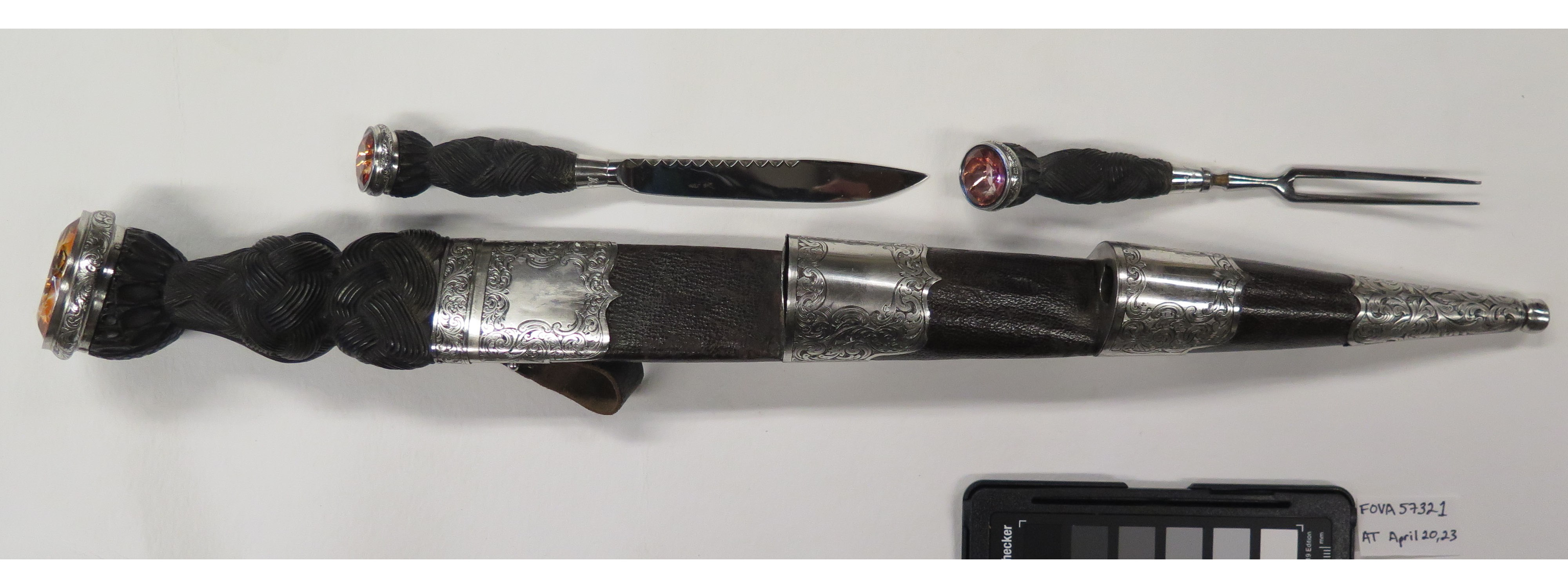 A dagger in a sheath, small knife and fork. All are dull and tarnished with orange gemstones on their hilts.