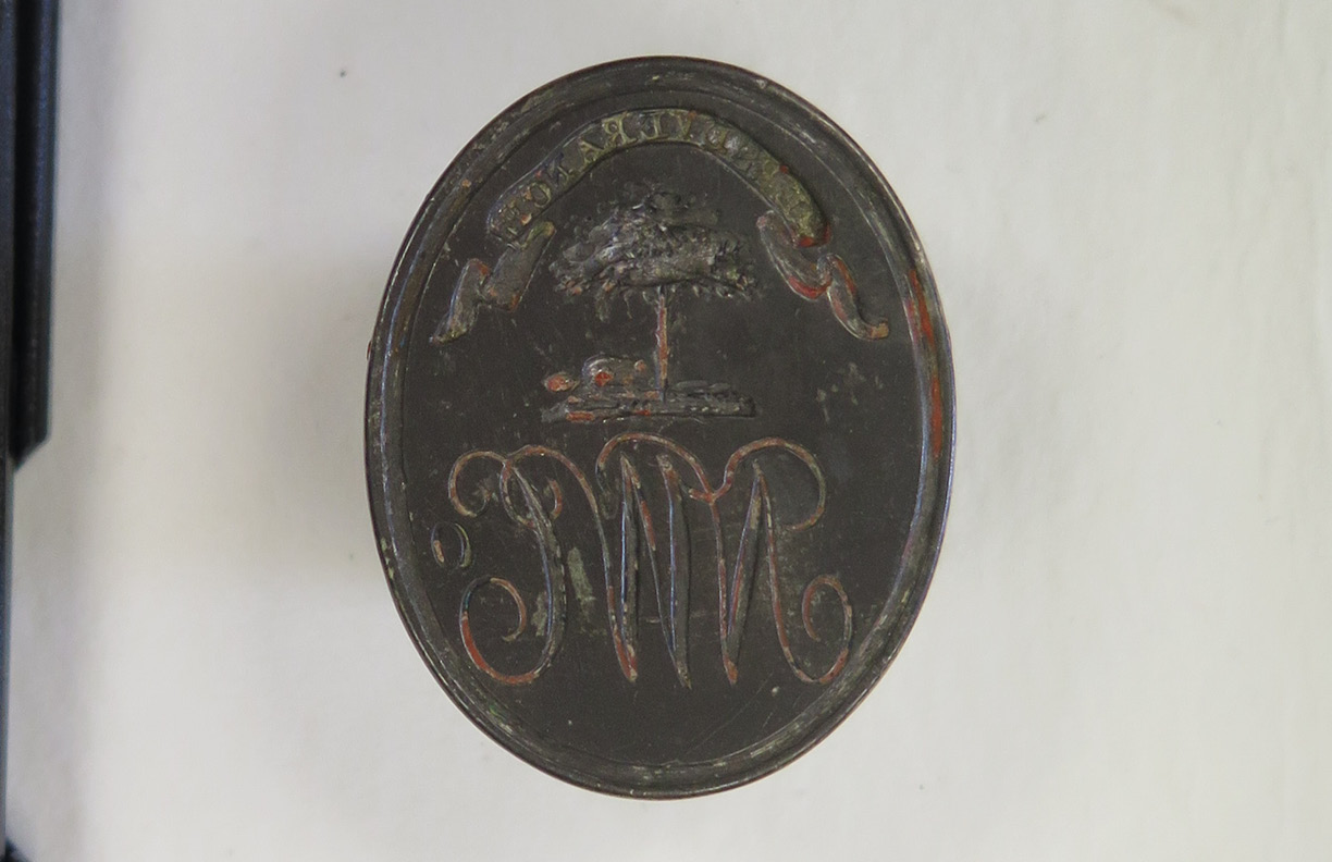 A metal seal with the letters NWC, a tree, and a banner with the word "Perseverance." The seal is darkened with age and grime.