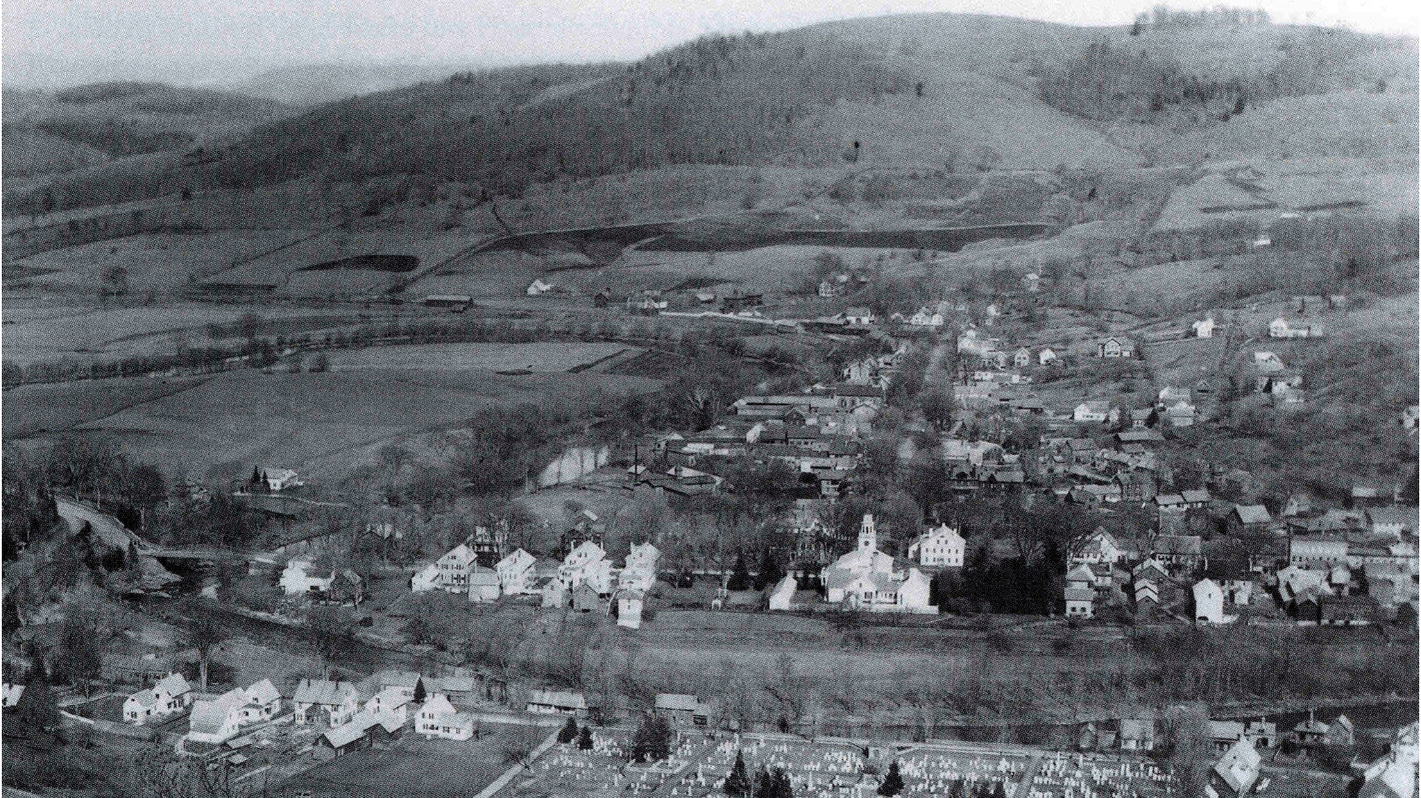 a black and white photo of a town in a valley with very few trees