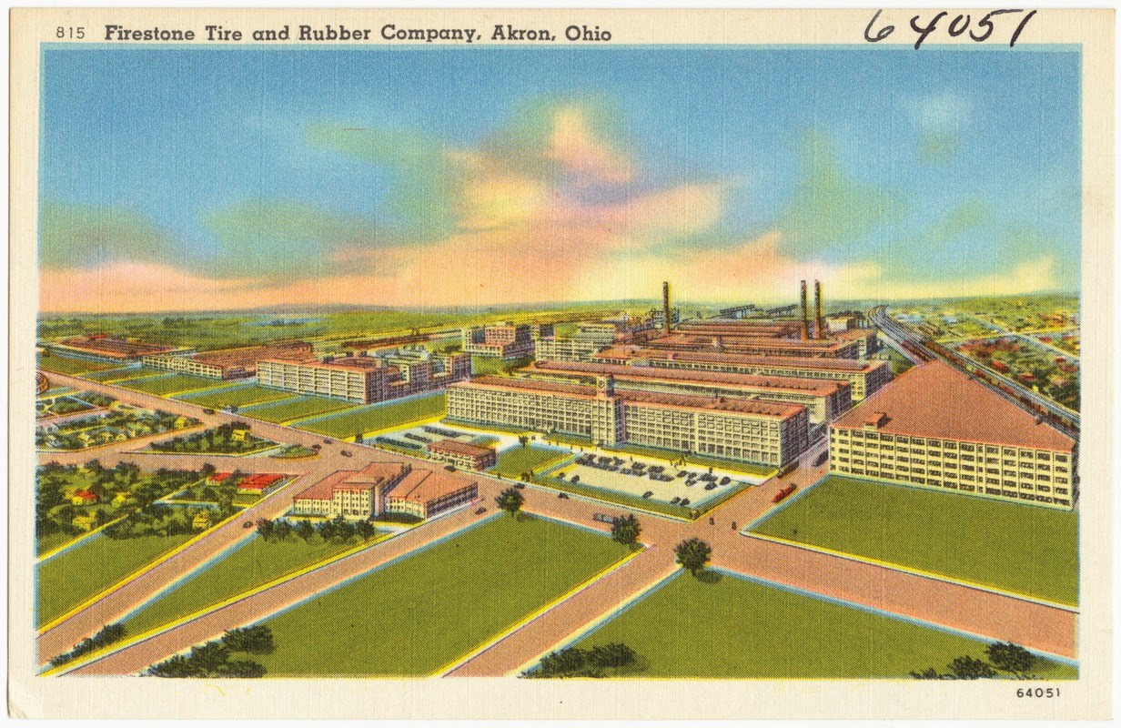 Color postcard illustration of bird’s eye view of blocky, multi-story factory buildings surrounded by a residential area. Three smokestacks spew smoke. Train tracks run alongside and through the complex. A white US Navy blimp flies overhead.