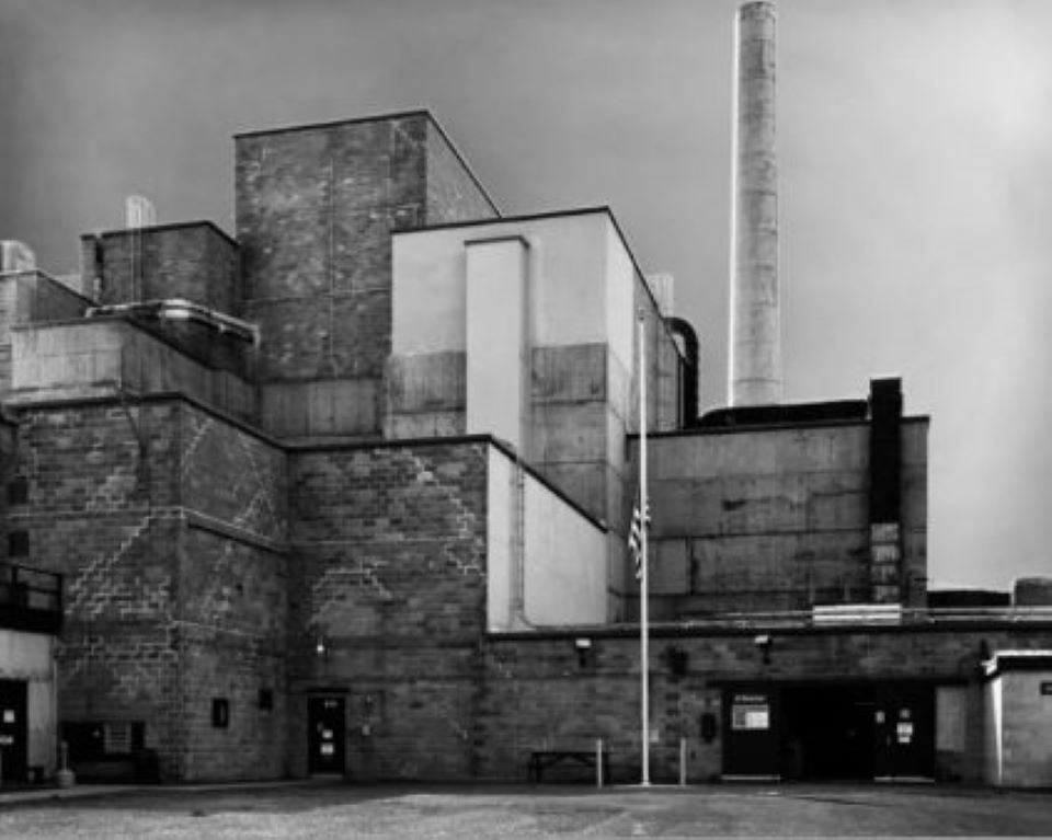 Black and white photo of brick factory buildings with a white chimney