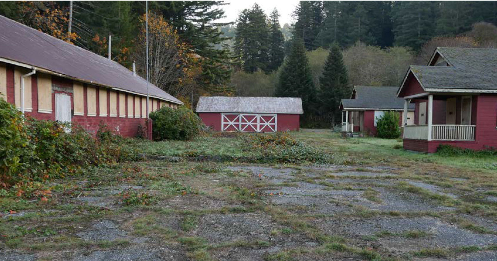 One-story buildings form a perimeter around an area of lawn and asphalt. Some shrubs grow at the foundations and a pond is in the center.